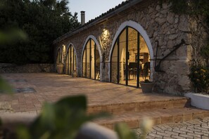 Un bâtiment en pierre doté de fenêtres en arc de cercle et d’une terrasse dallée.