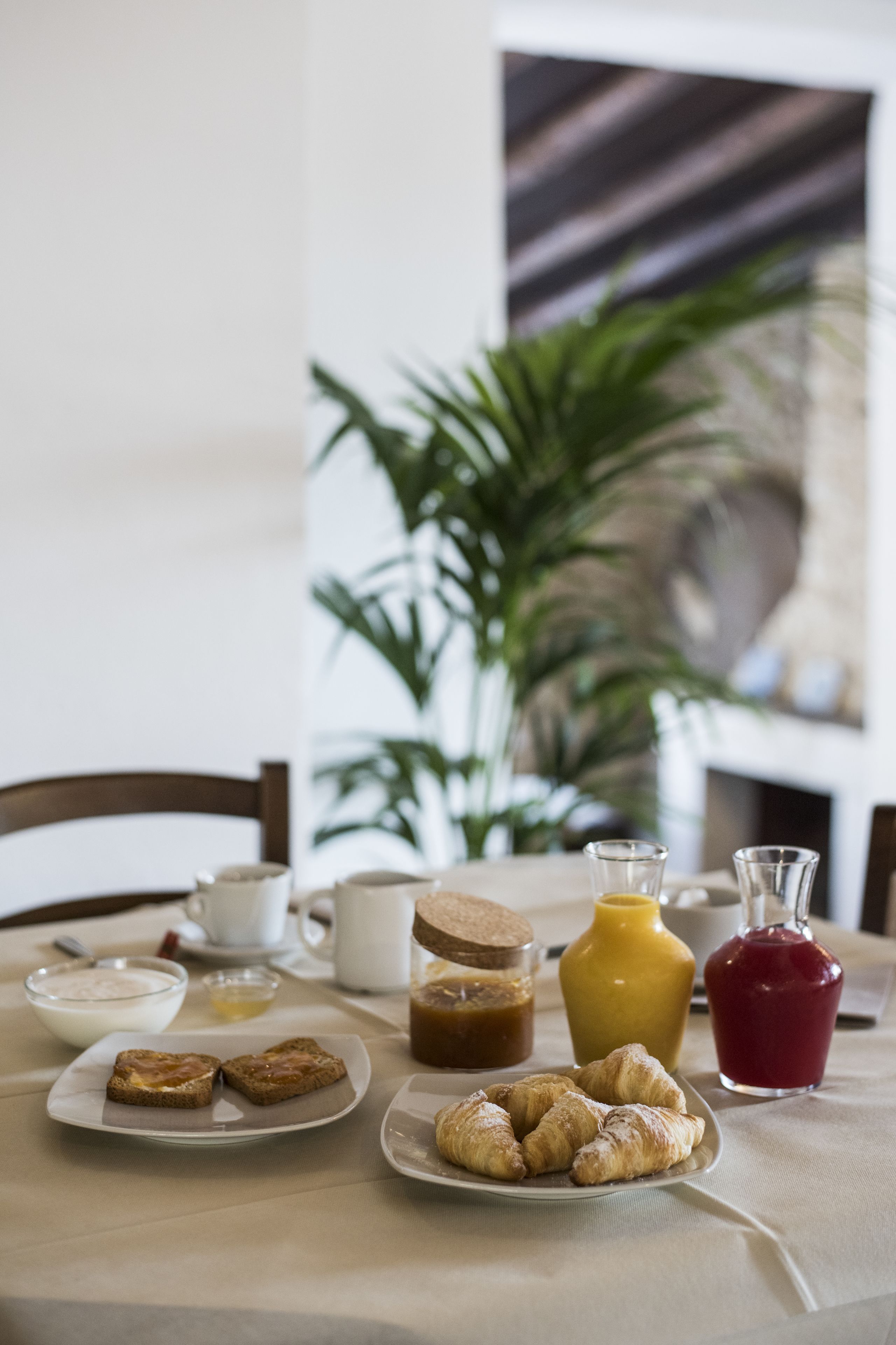 A breakfast table with croissants, a bottle of juice, a jar of jam, and a coffee pot.