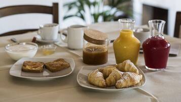 A breakfast table with croissants, a bottle of juice, a jar of jam, and a coffee pot.
