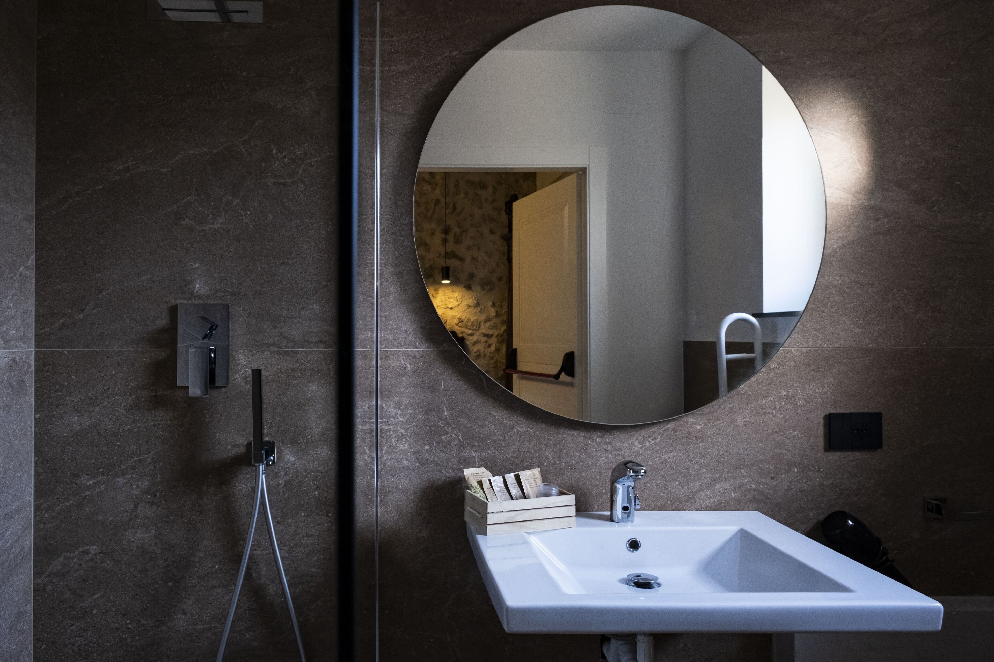 Ein Badezimmer mit einem weißen Waschbecken, einem runden Spiegel und einer auf einem Stativ montierten Kamera.