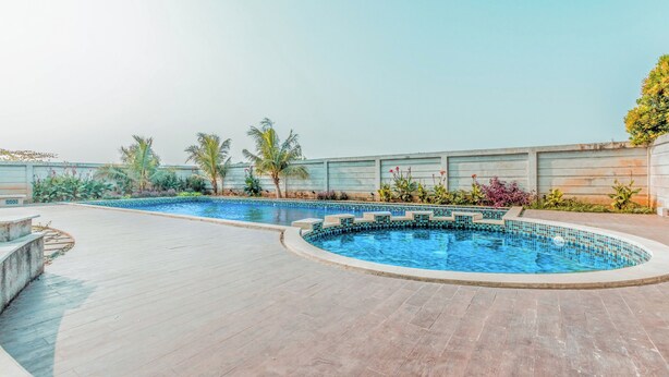 Une piscine dont le bord est revêtu de carrelage, entourée d’une terrasse en bois et de palmiers.