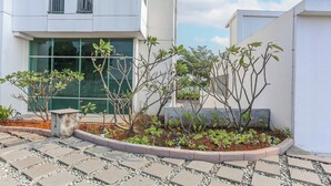 Un bâtiment moderne doté d’une allée pavée, d’un petit jardin planté de jeunes arbres et surplombé d’un ciel dégagé.
