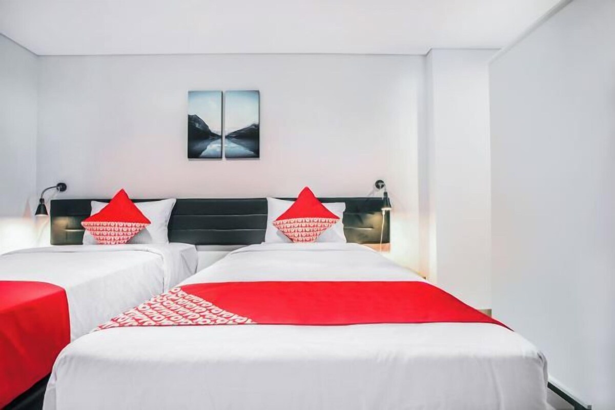 A hotel room with two beds, a red and white bedspread, and a wall-mounted artwork.