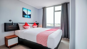 Une chambre d’hôtel moderne avec un grand lit, une table de chevet, une lampe fixée au mur et une vue sur la ville par la fenêtre.