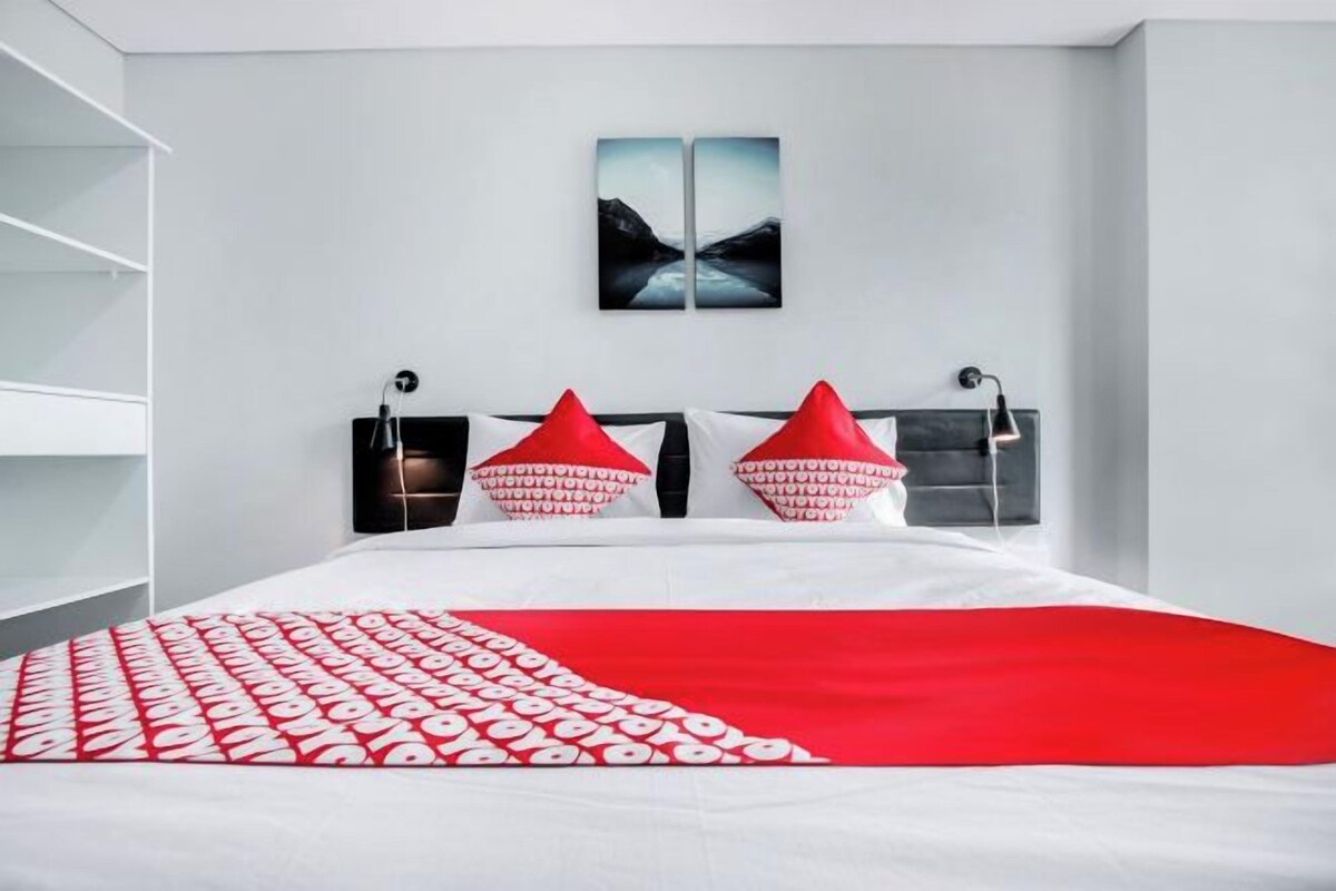 A modern bedroom with a bed, two red pillows, a white and red bedspread, and a wall-mounted artwork.