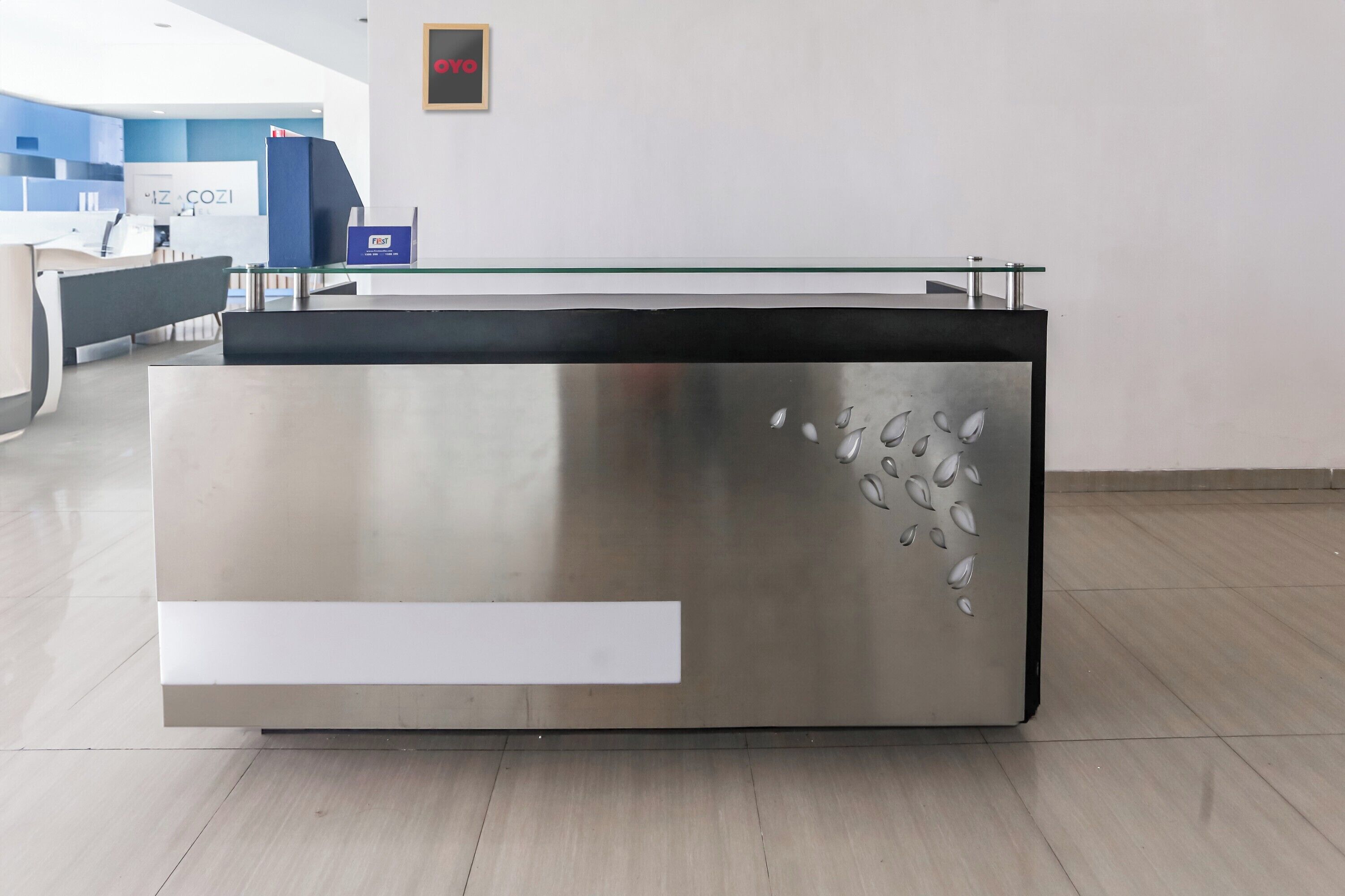 En receptionsdisk med glasplade og metalfinish, placeret i en moderne lobby med en blå accentvæg og et skilt med teksten "IZ COZI".