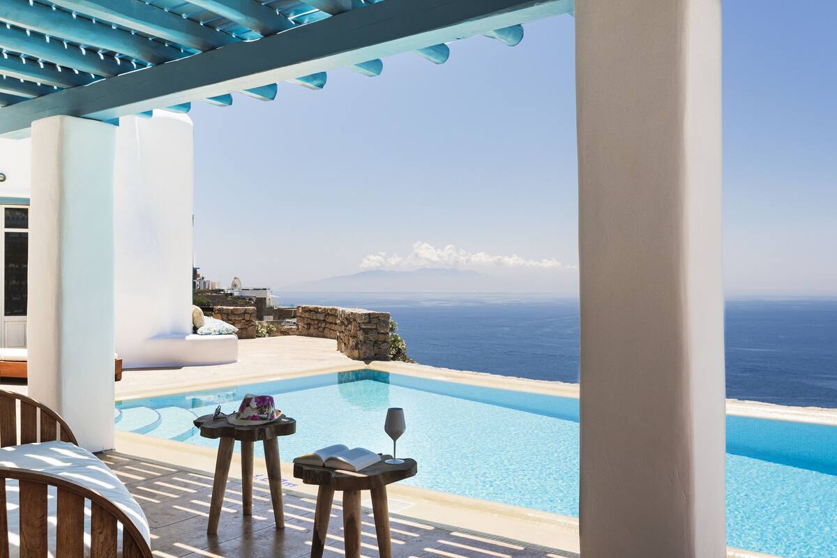 A poolside area with a view of the sea, a stone wall, and a white building.
