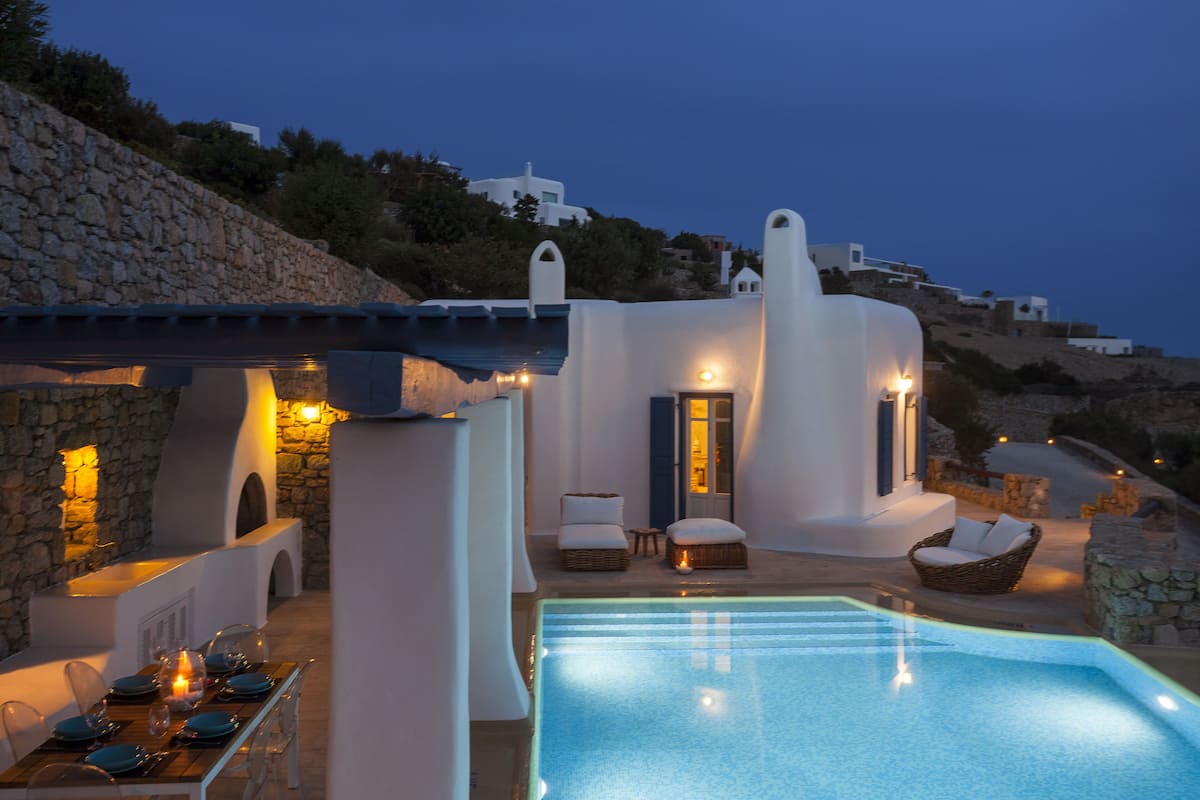 A poolside area with a dining setup, a small seating area with cushions, and a stone wall.