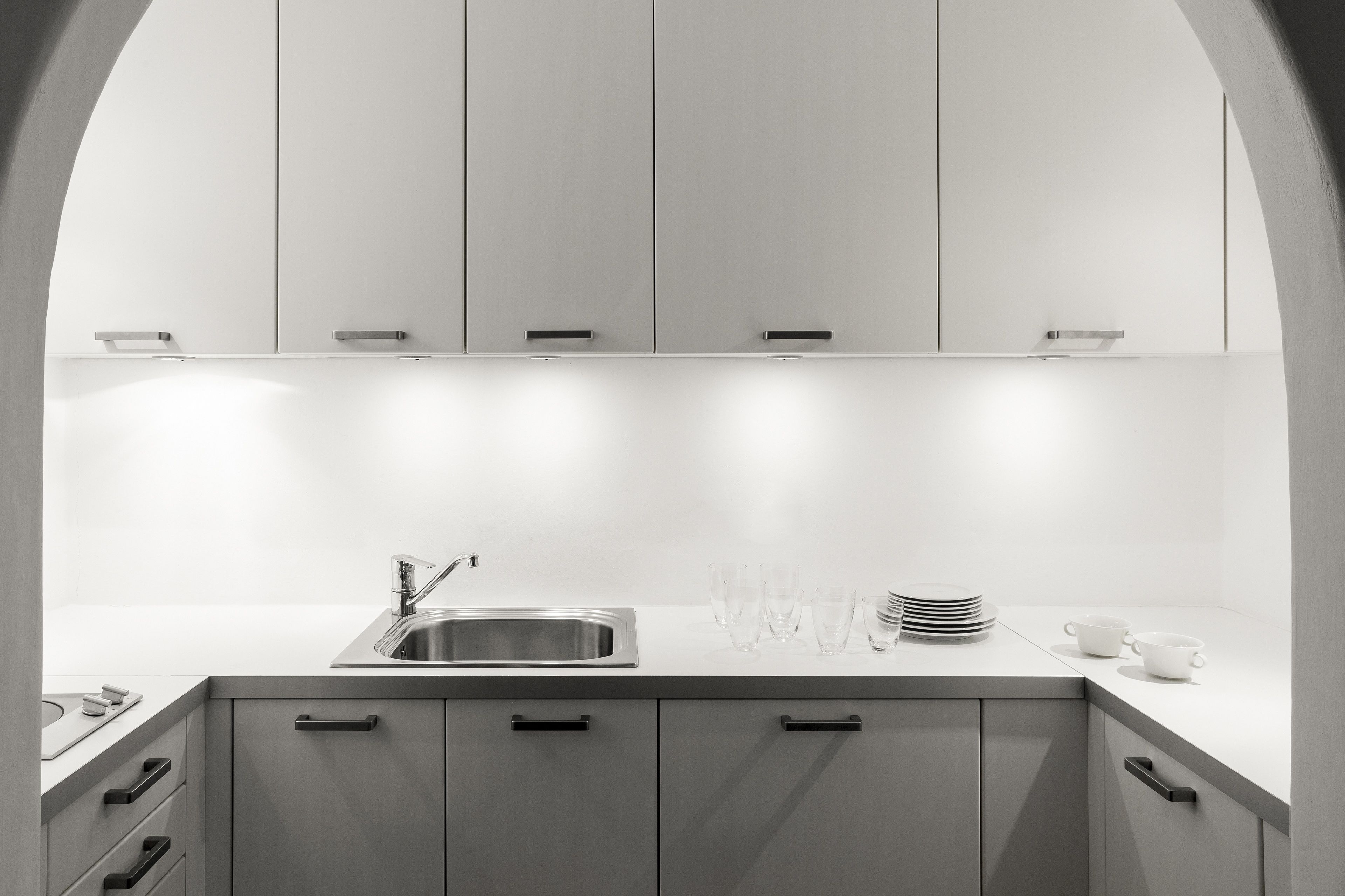 A modern kitchen with white cabinets, a stainless steel sink, and a countertop with stacked plates and glasses.