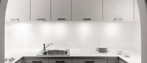 A modern kitchen with white cabinets, a stainless steel sink, and a countertop with stacked plates and glasses.
