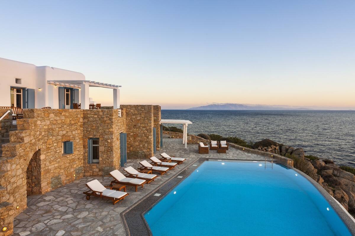 A poolside area with lounge chairs, a stone building, and a view of the sea.