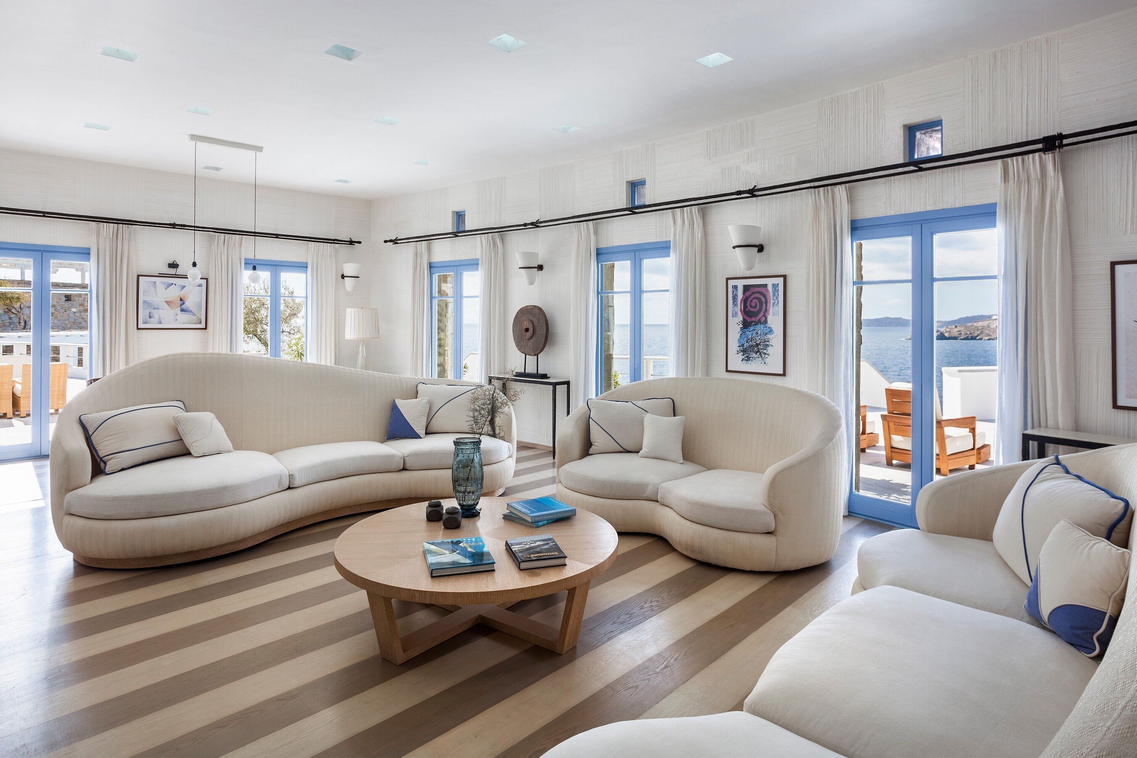 A spacious living room with a large L-shaped sofa, a round coffee table, and a view of the sea through large windows.