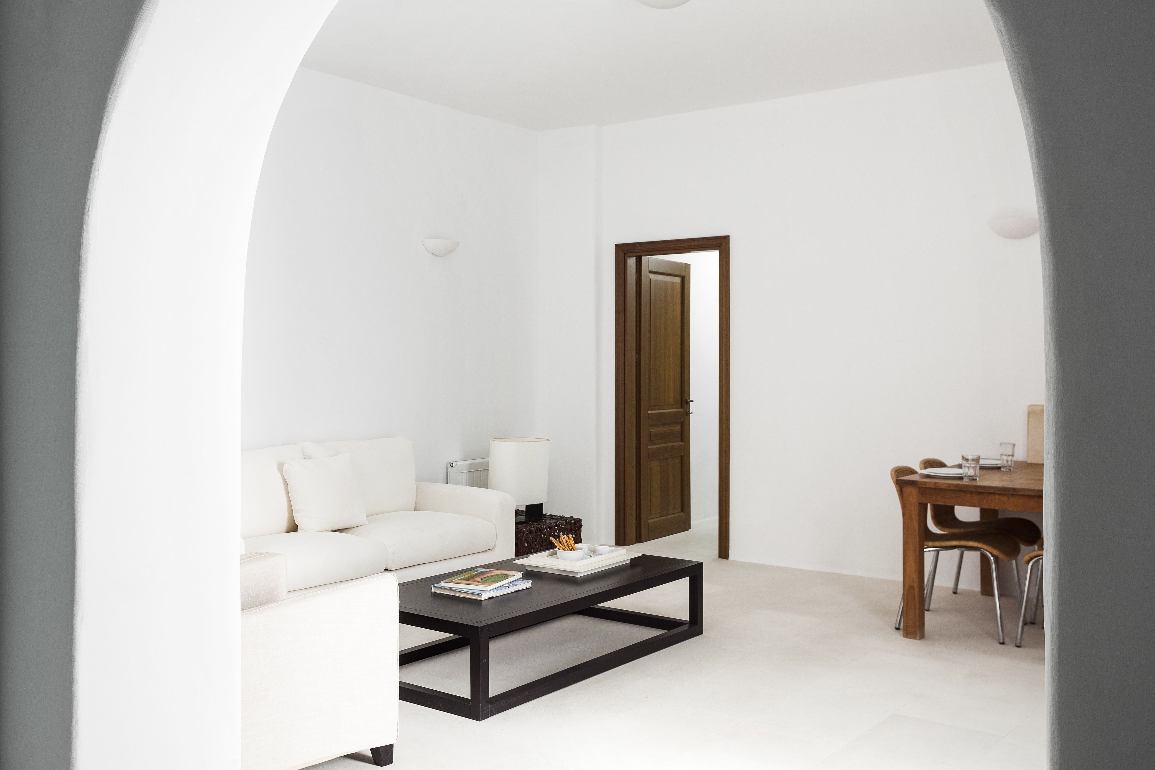 A modern living room with a white sofa, a black coffee table, and a wooden dining table with chairs.