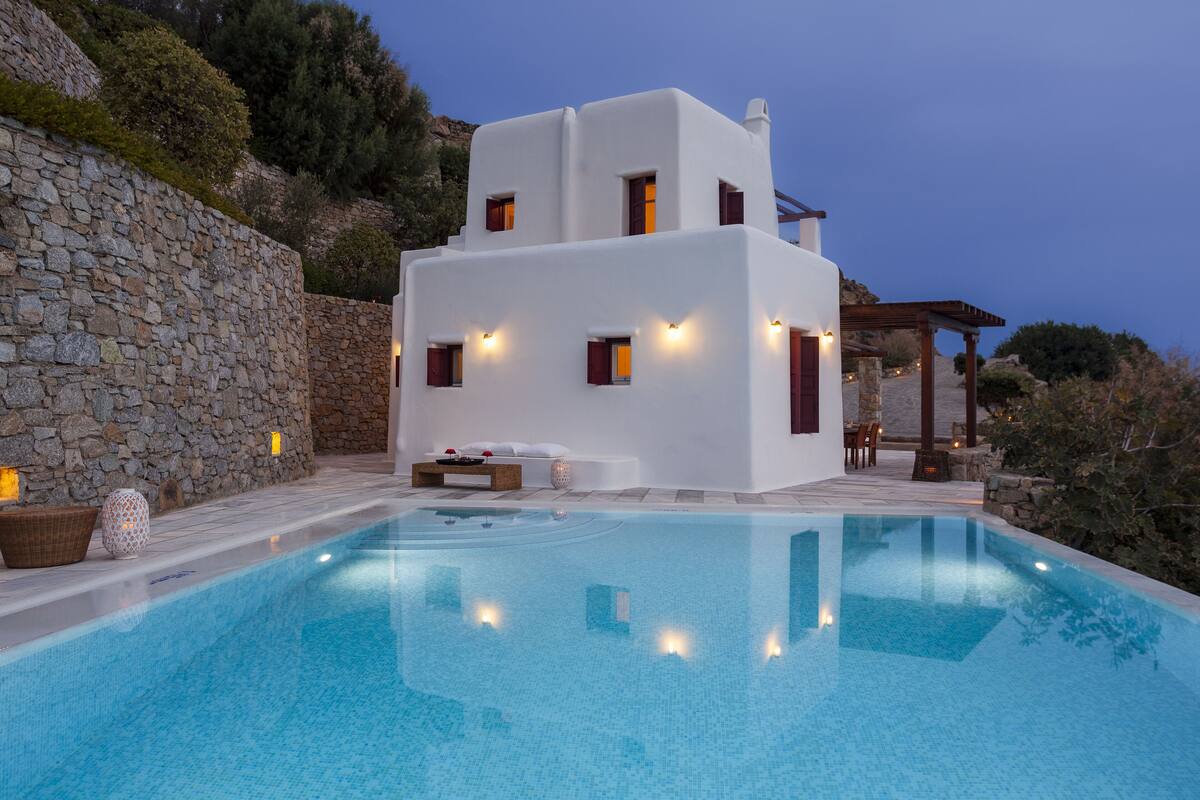 A modern white building with a pool, stone wall, and outdoor seating area.