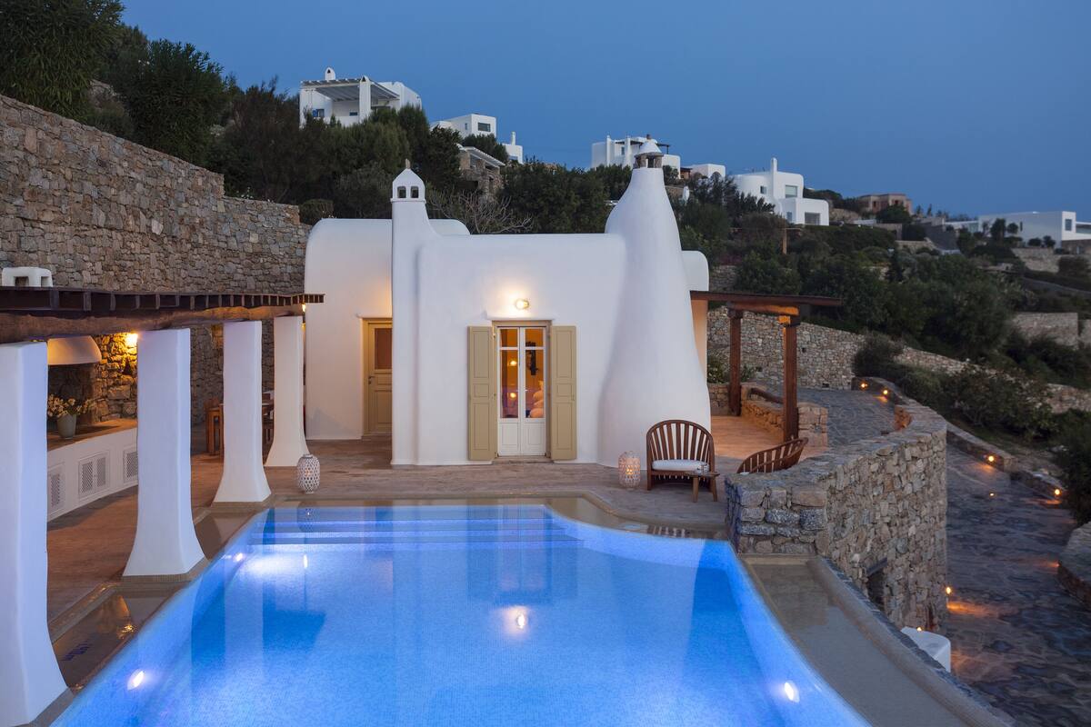 A poolside area with a white building, stone walls, and a view of the surrounding landscape.