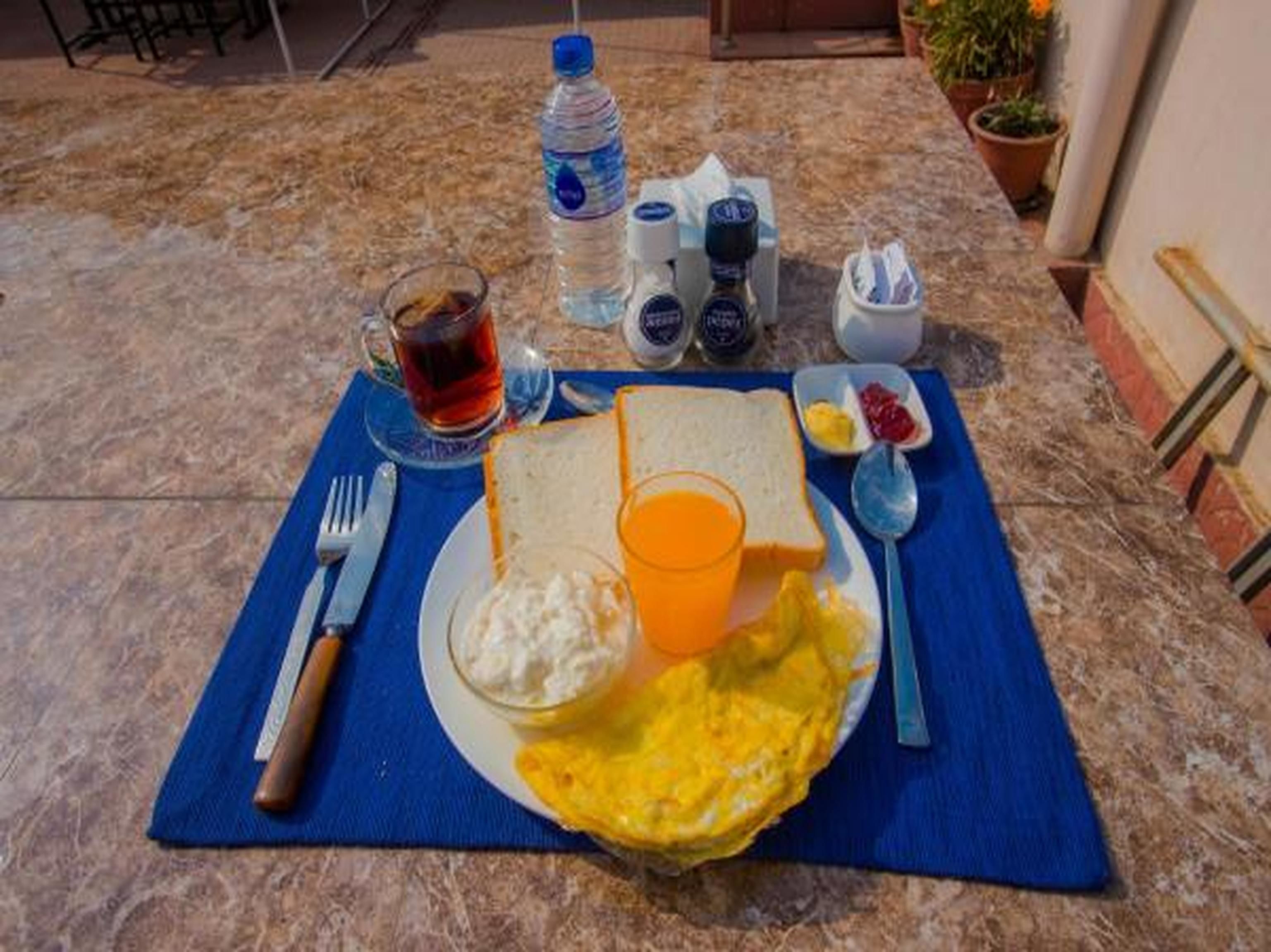 A breakfast setting with toast, scrambled eggs, a glass of orange juice, a cup of tea, and condiments on a marble table.