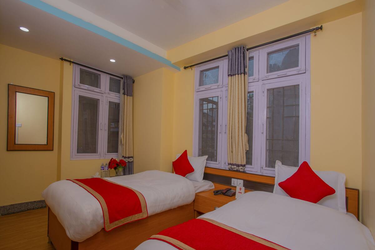 Une chambre d’hôtel avec deux lits, un plancher en bois, un miroir et une fenêtre avec des rideaux.
