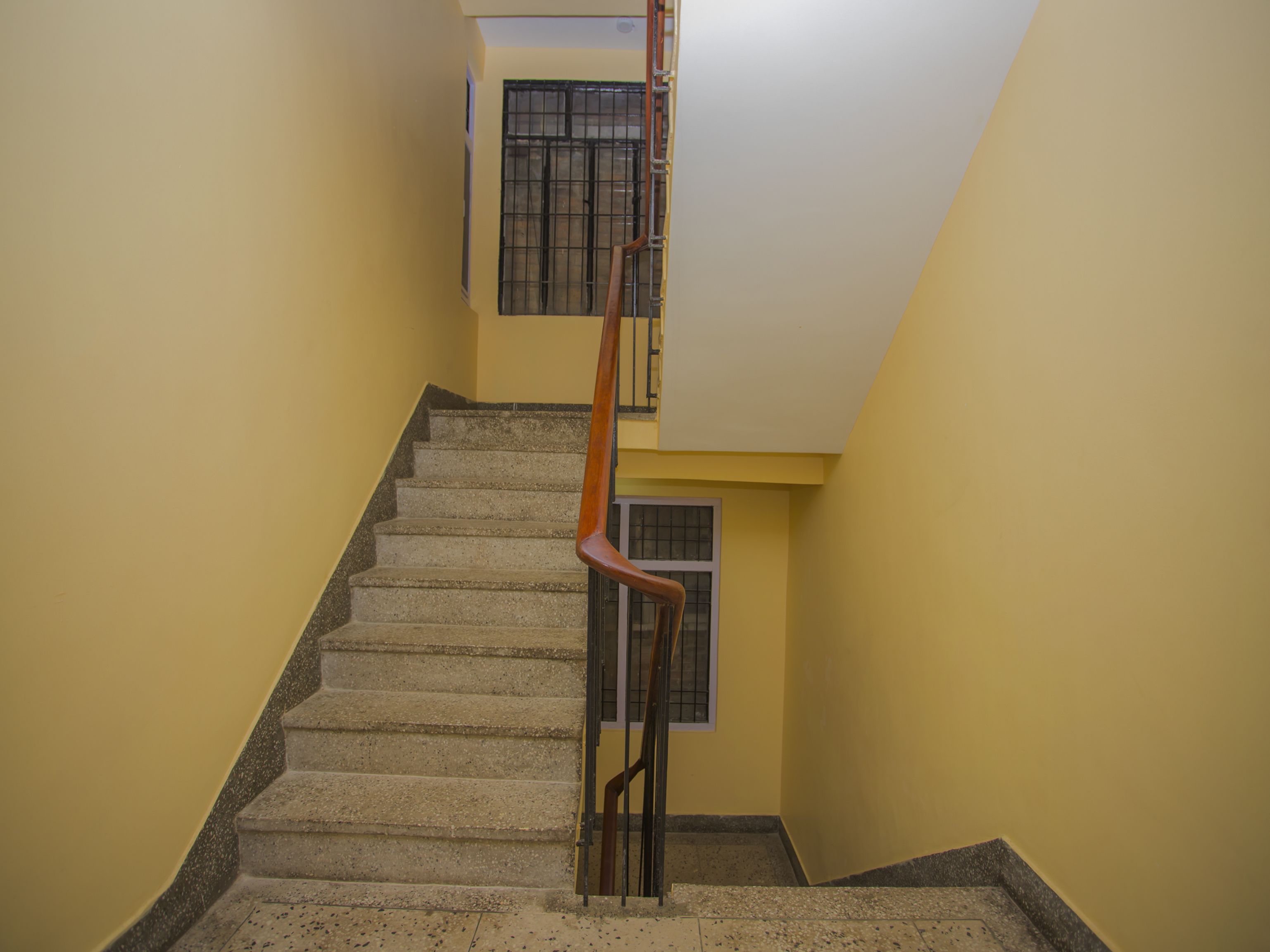 A staircase with a wooden handrail and a concrete floor, leading to a room with a window and a door.