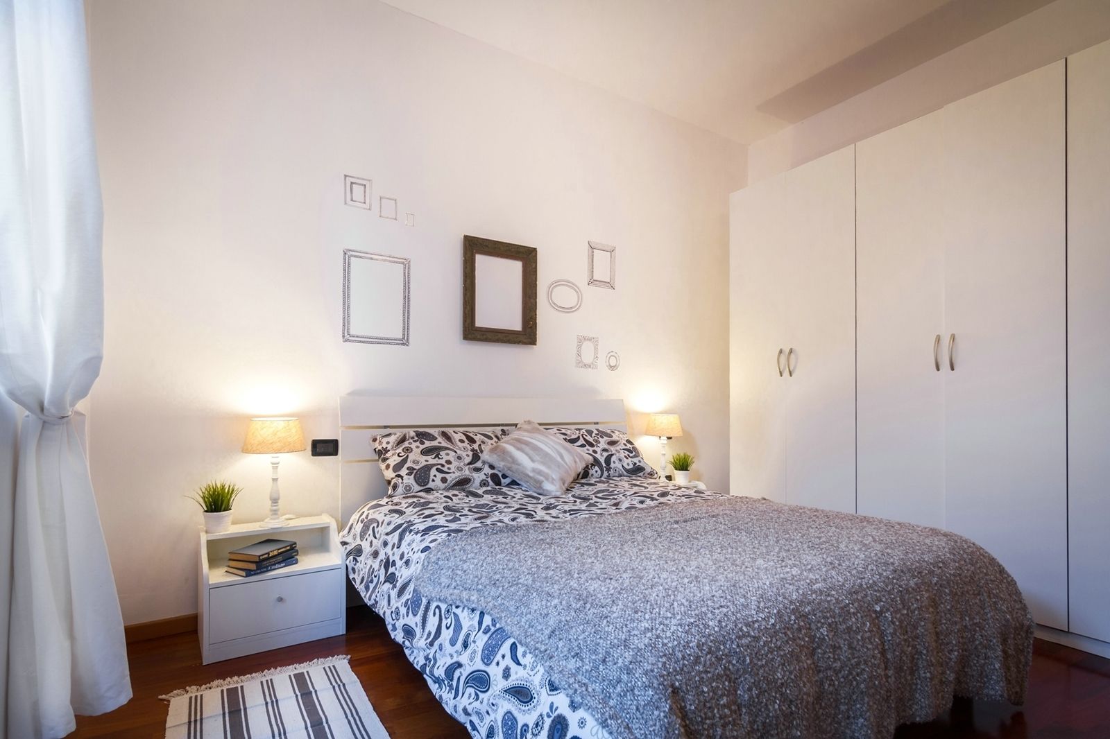 A bedroom with a bed, nightstands, a lamp, a potted plant, and a wardrobe.