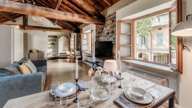 A dining area with a wooden table set for a meal, a stone wall, and a view of a courtyard. - La Corte delle Rondini (Como)