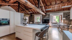 A spacious kitchen with a large island, wooden beams on the ceiling, and a stone wall. - La Corte delle Rondini (Como)