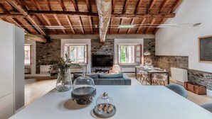 A spacious living area with a stone fireplace, wooden ceiling beams, and a modern dining table. - La Corte delle Rondini (Como)