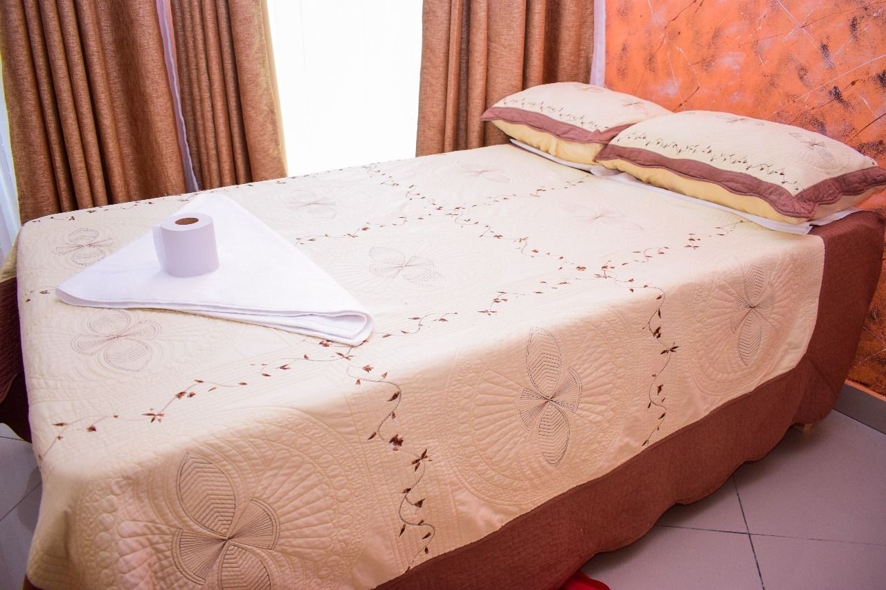 A neatly made bed with a floral patterned bedspread, a rolled-up towel, and a pillow with a decorative cover.