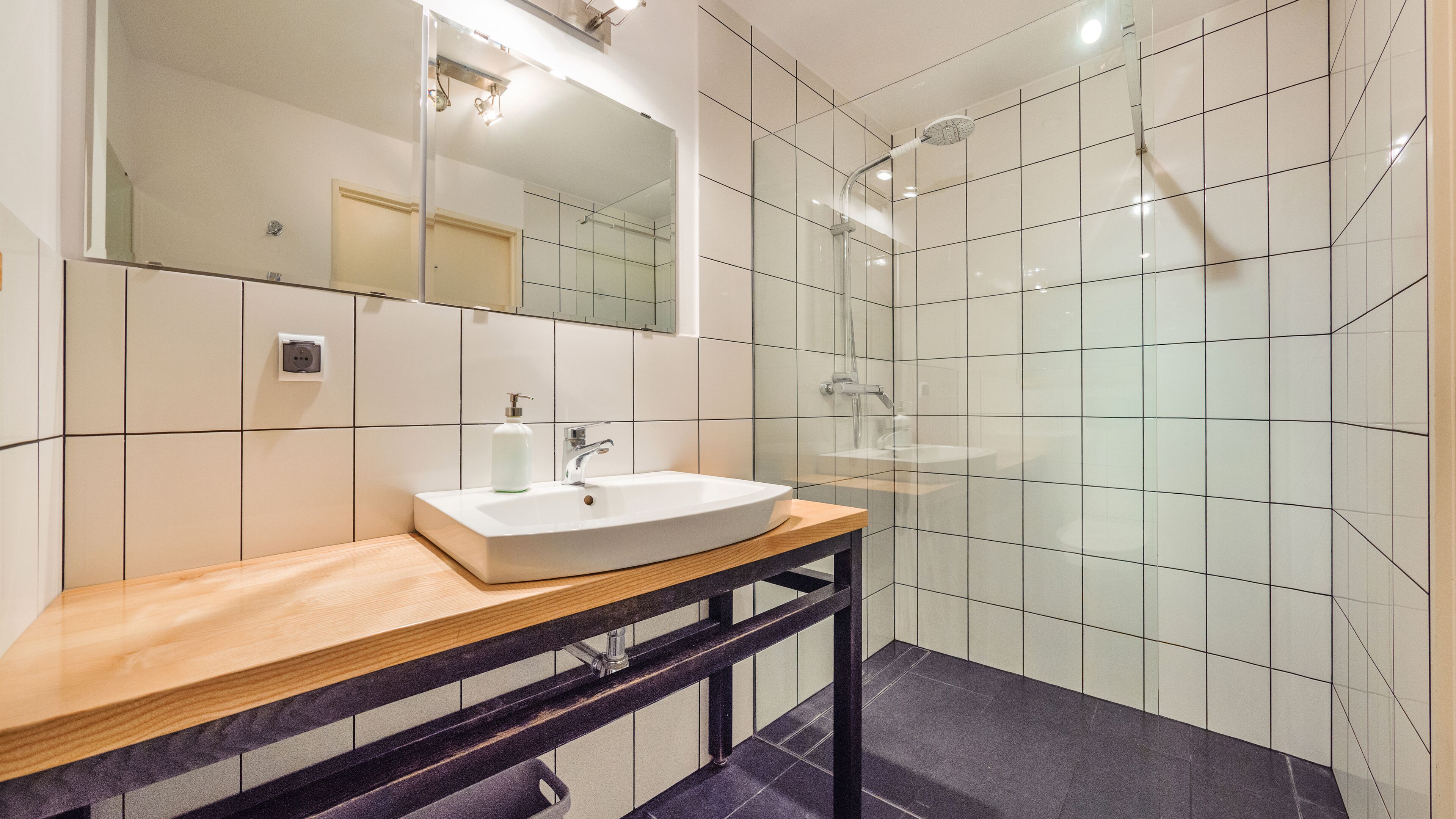 Un baño moderno con un lavamanos blanco, encimera de madera y mampara de ducha de vidrio.