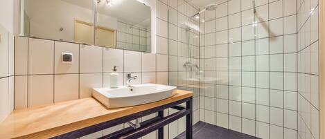 Un baño moderno con un lavamanos blanco, encimera de madera y mampara de ducha de vidrio.