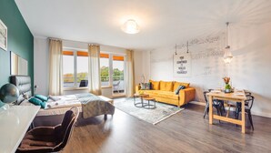 Ein modernes Wohnzimmer mit einer Couch, einem Esstisch und einem großen Fenster mit Blick ins Freie.