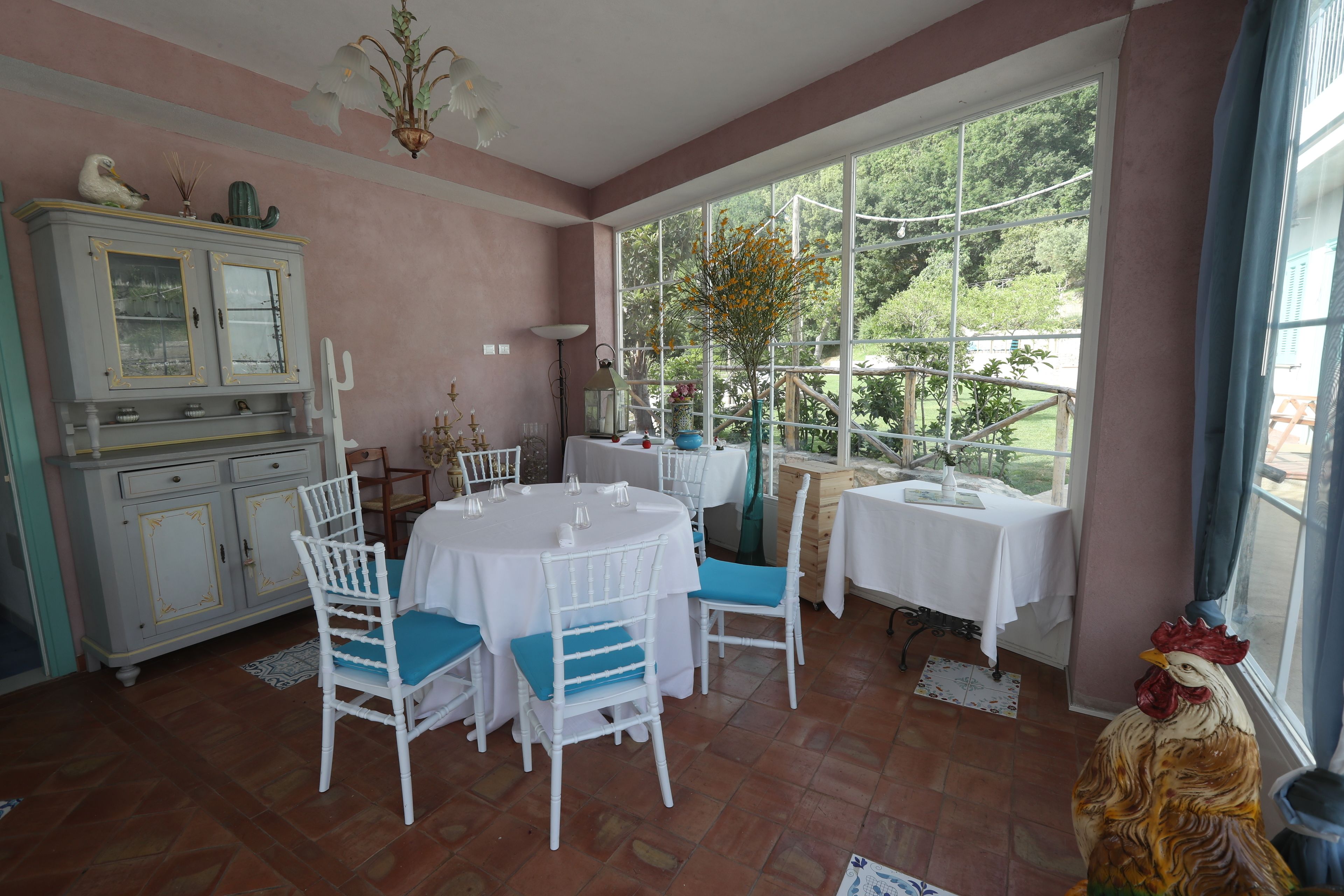 Un coin repas avec une table ronde, des chaises blanches et une vue sur un jardin grâce à de grandes fenêtres.
