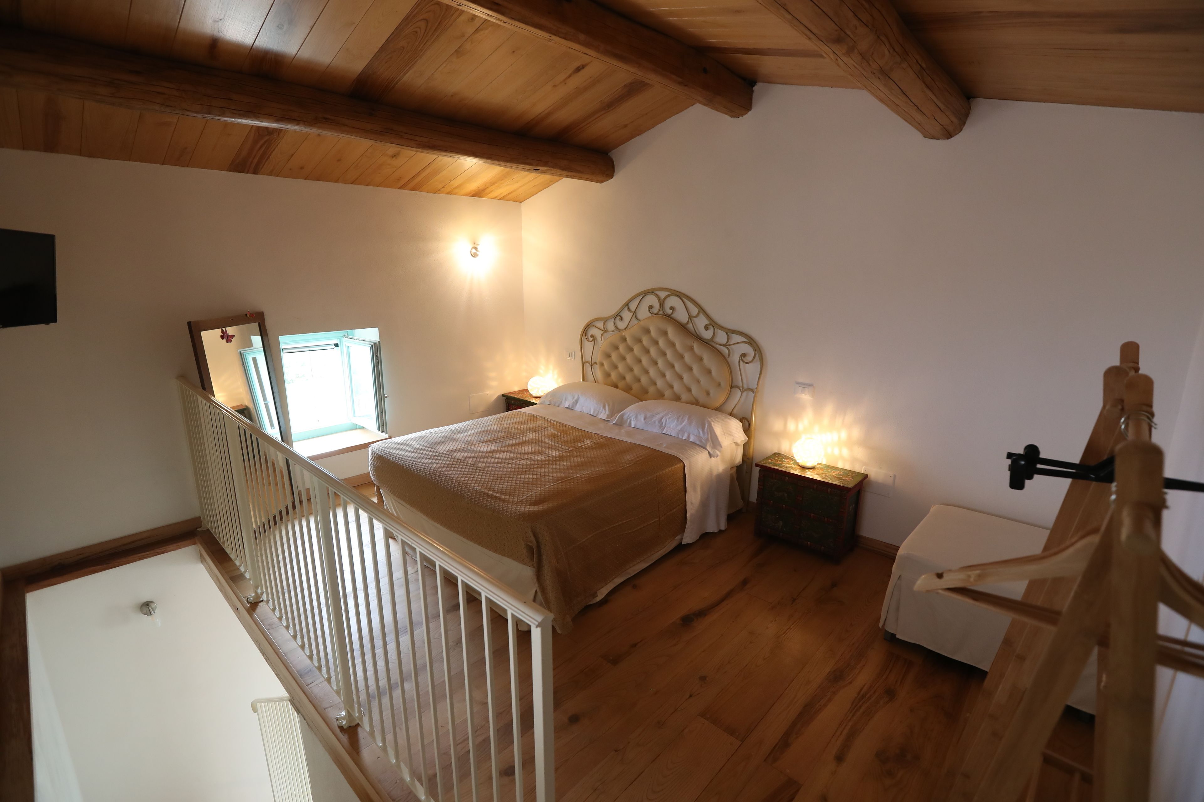 A bedroom with a wooden ceiling, a bed with a headboard, bedside tables, and a crib.