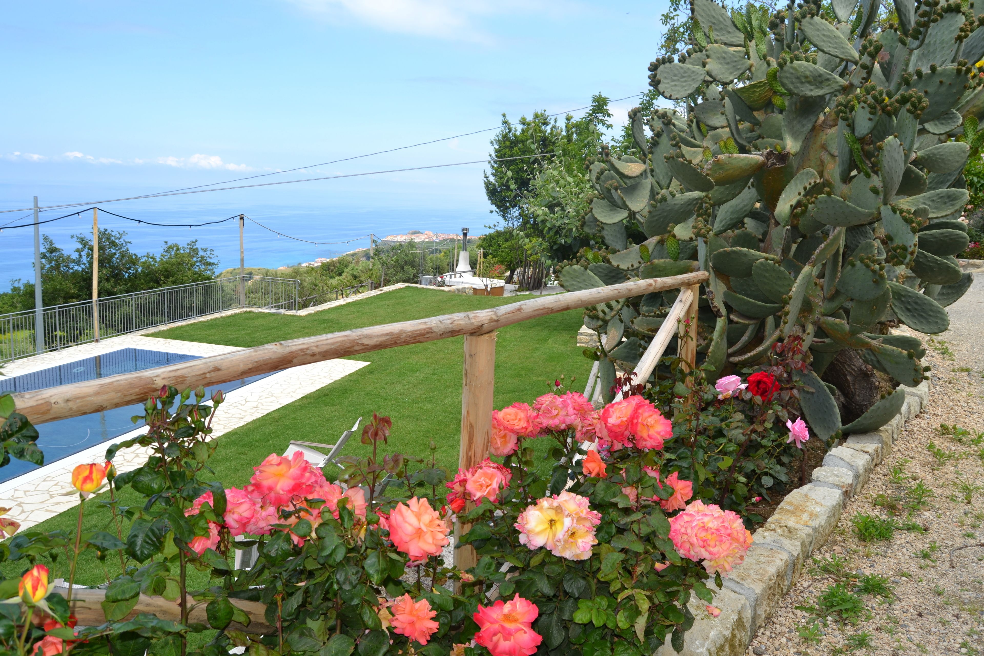 Un jardín con piscina, cerca de madera y vista al mar.