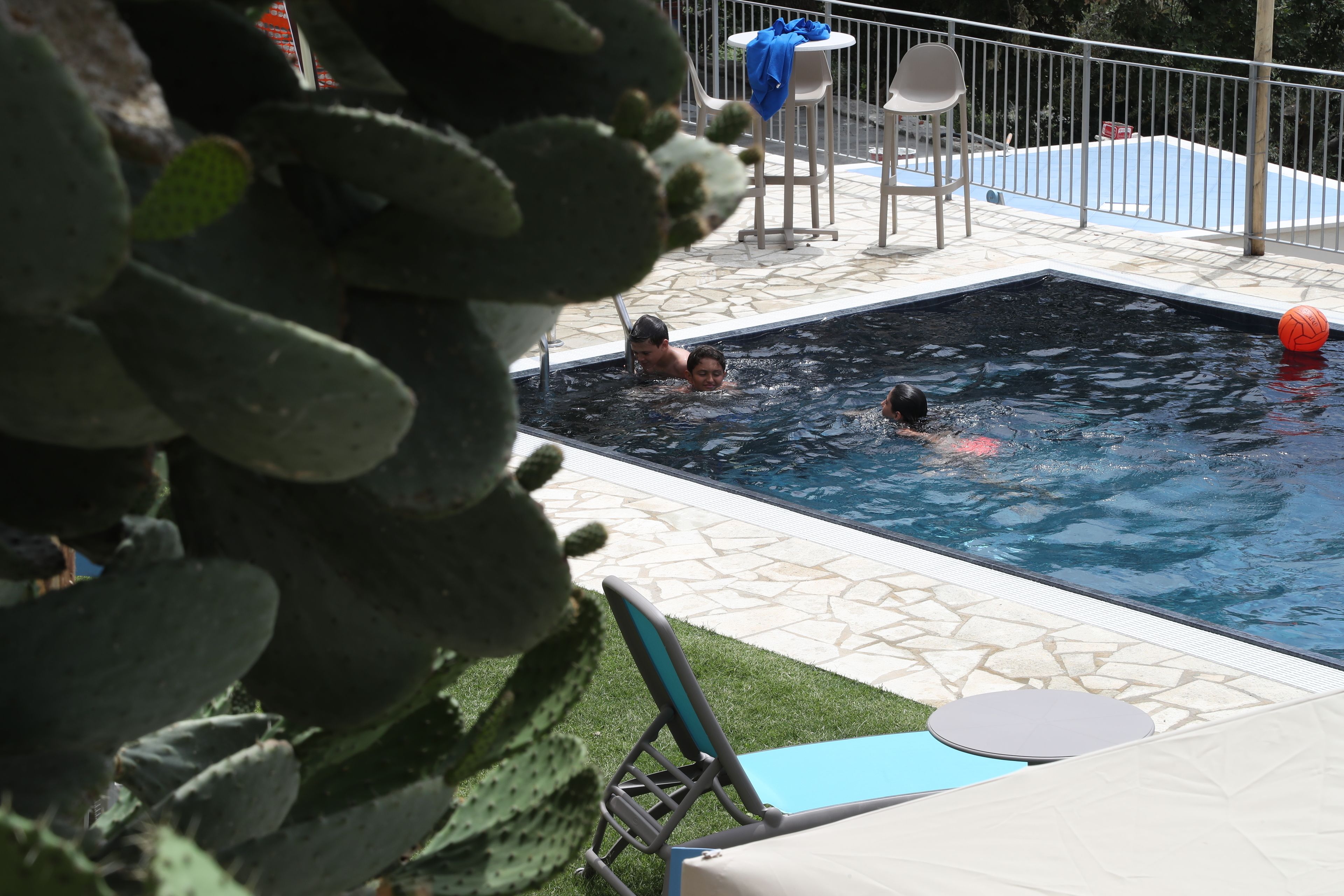 Una piscina con alcune persone a nuotare, circondata da un patio con sedie e un tavolo.