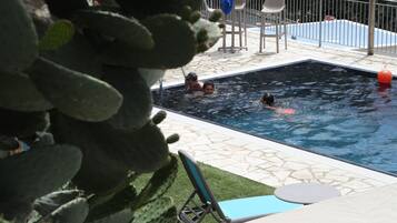Una piscina con alcune persone a nuotare, circondata da un patio con sedie e un tavolo.