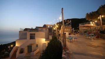 Un bâtiment moderne doté d’un escalier menant à une terrasse, d’un espace extérieur aménagé pour s’asseoir et de guirlandes lumineuses.