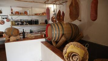Cocina rústica con barriles de madera, estantes con botellas y carne colgando.