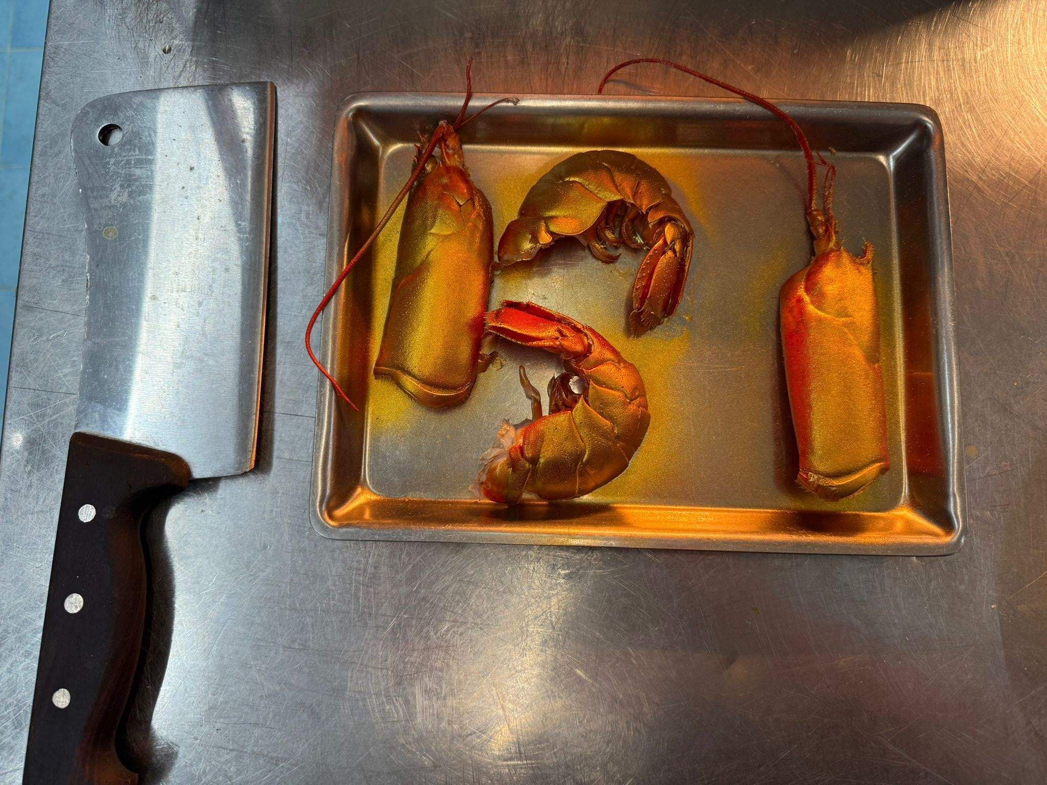 Una bandeja de metal con tres langostas cocidas sobre una superficie de acero inoxidable.