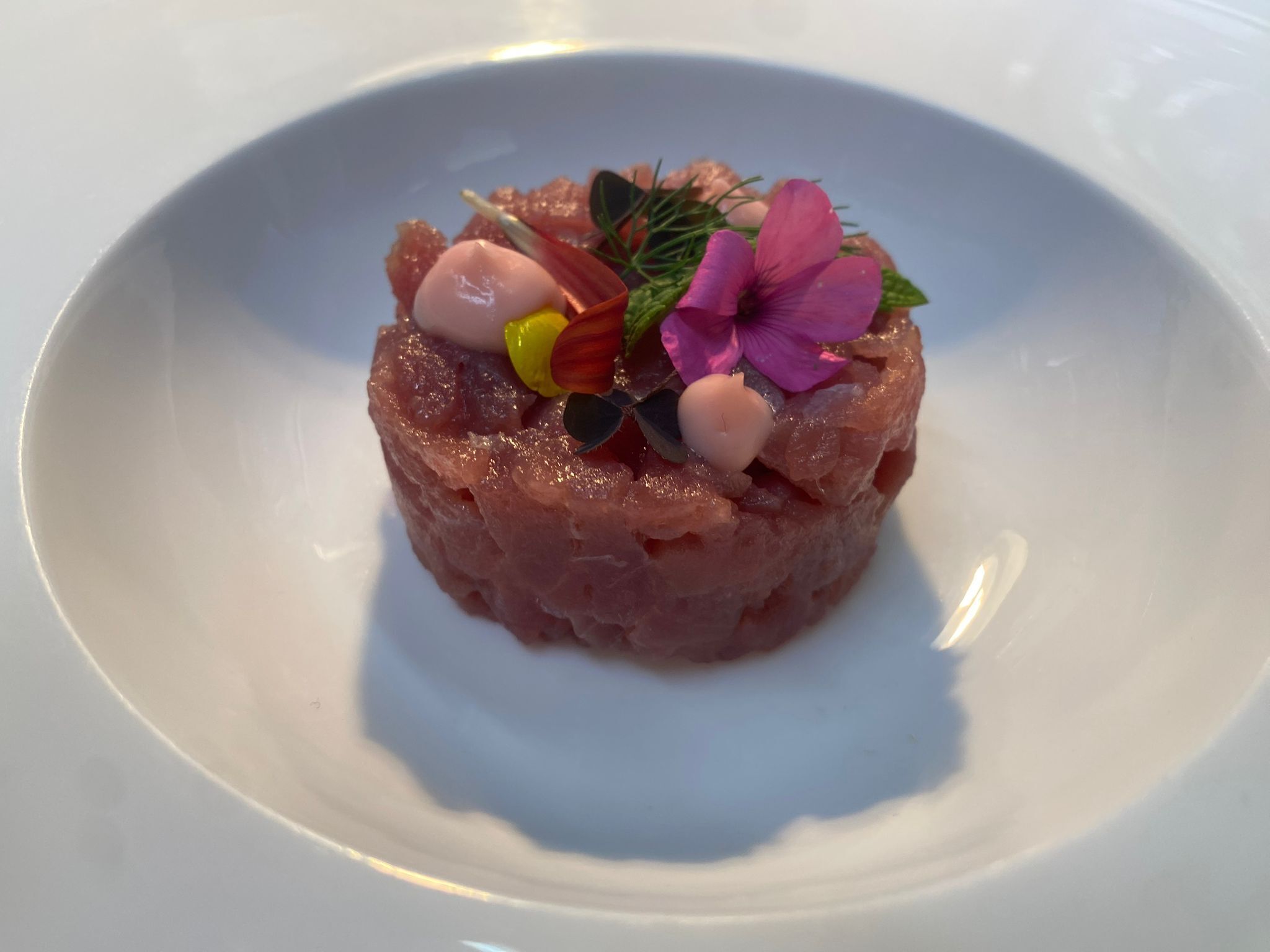 Une assiette blanche avec une portion de nourriture au centre, agrémentée de fleurs et d’herbes aromatiques.