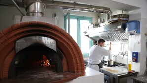 Eine Küche mit großem Backofen aus Ziegeln, Edelstahlgeräten und einem Fenster mit türkisumrandeten Details.