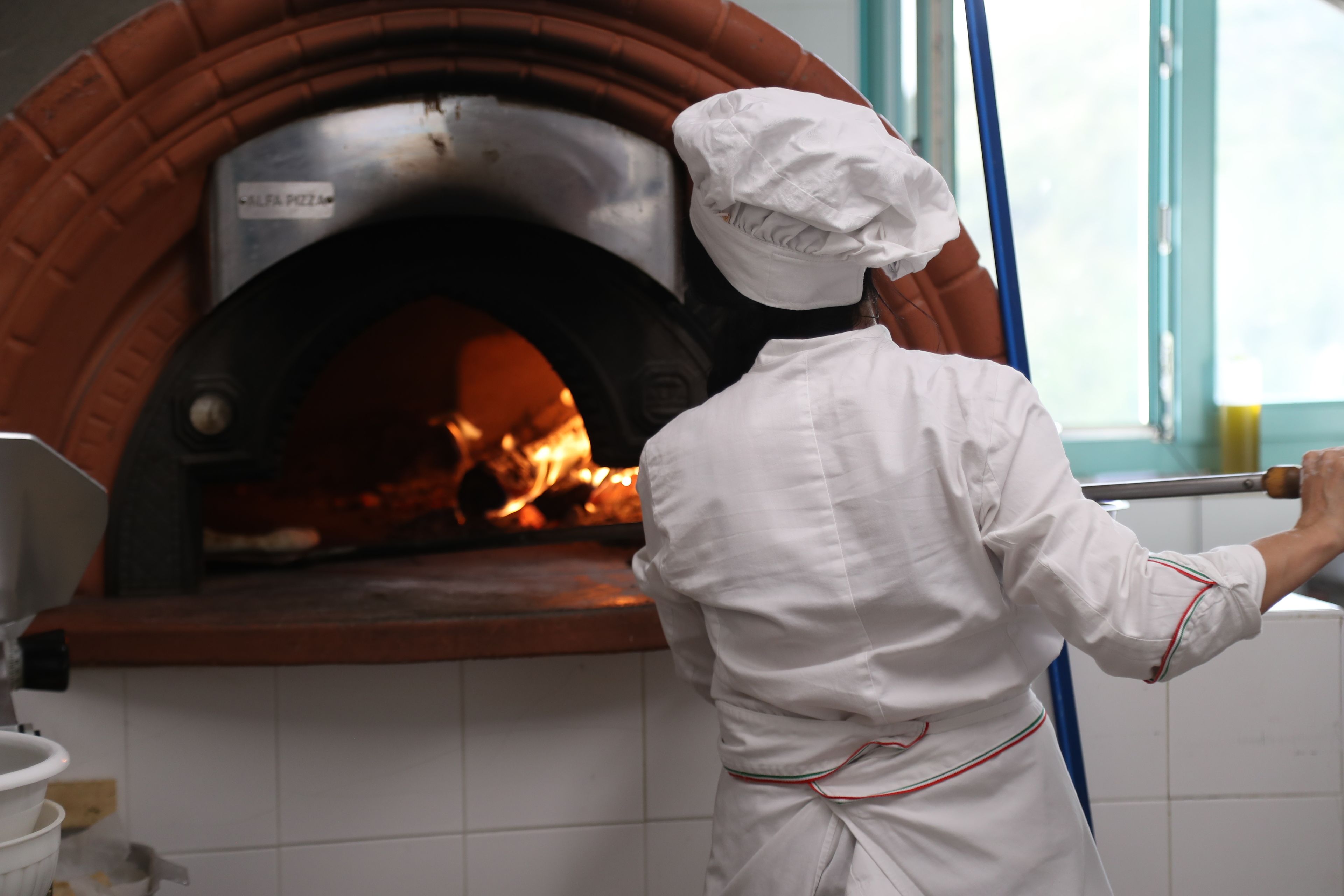 Ein Koch in weißer Uniform reinigt einen Backofen aus Ziegeln.