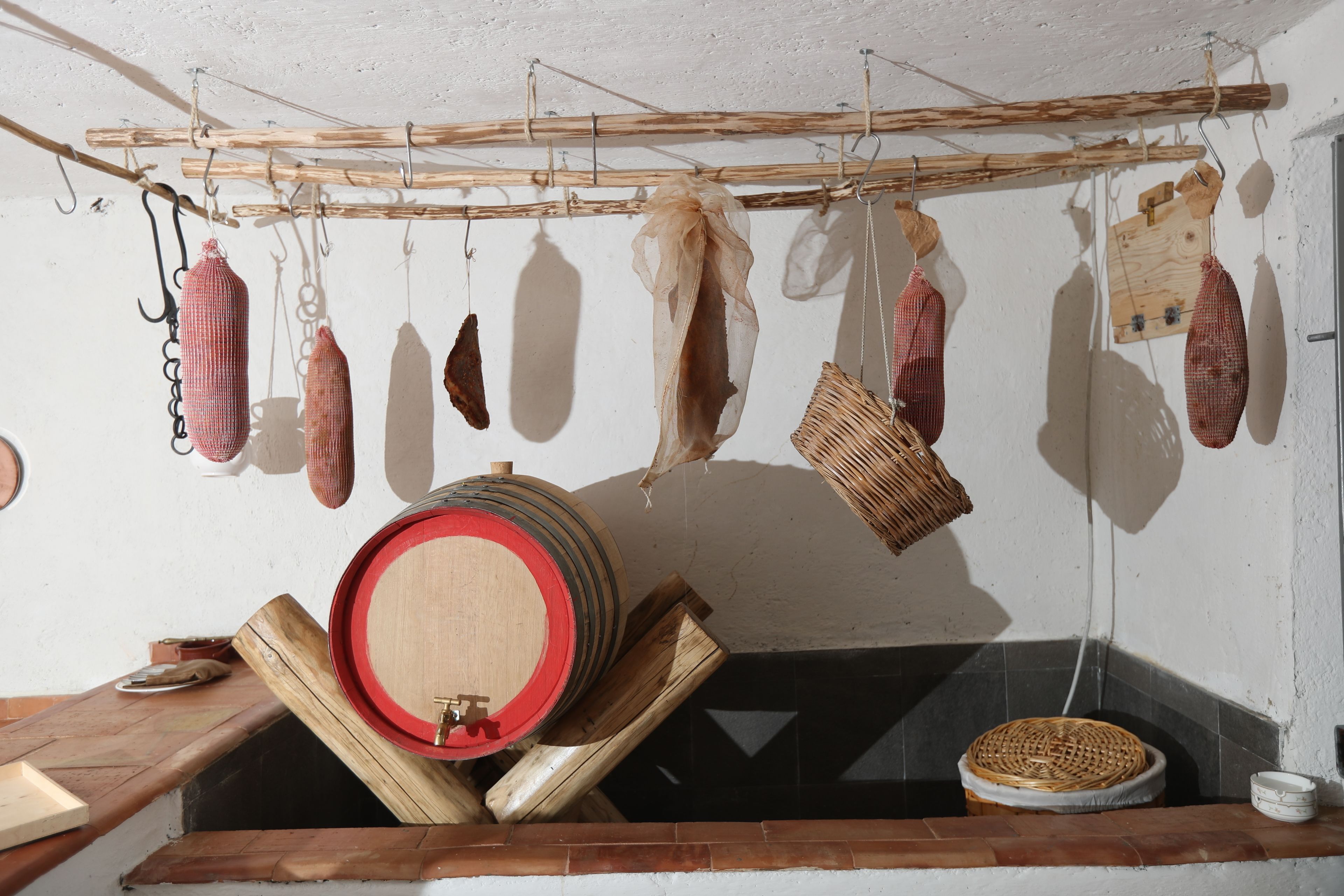Una cucina rustica con carne appesa, una botte di legno e un cesto di vimini.