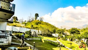 A residential area with a grassy yard, a small pond, and a person walking. - Van Durga Villas & Suites Katra (Reasi)