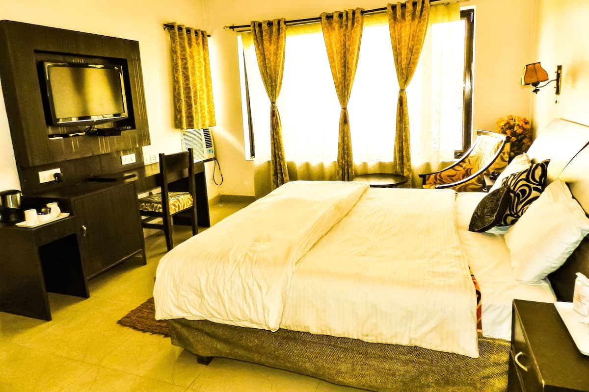 Quarto de hotel com uma cama, uma escrivaninha com cadeira, televisão e uma janela com cortinas.