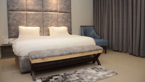 A modern bedroom with a large bed, a padded headboard, a bench, and a chair. - Van Durga Villas & Suites Katra (Reasi)