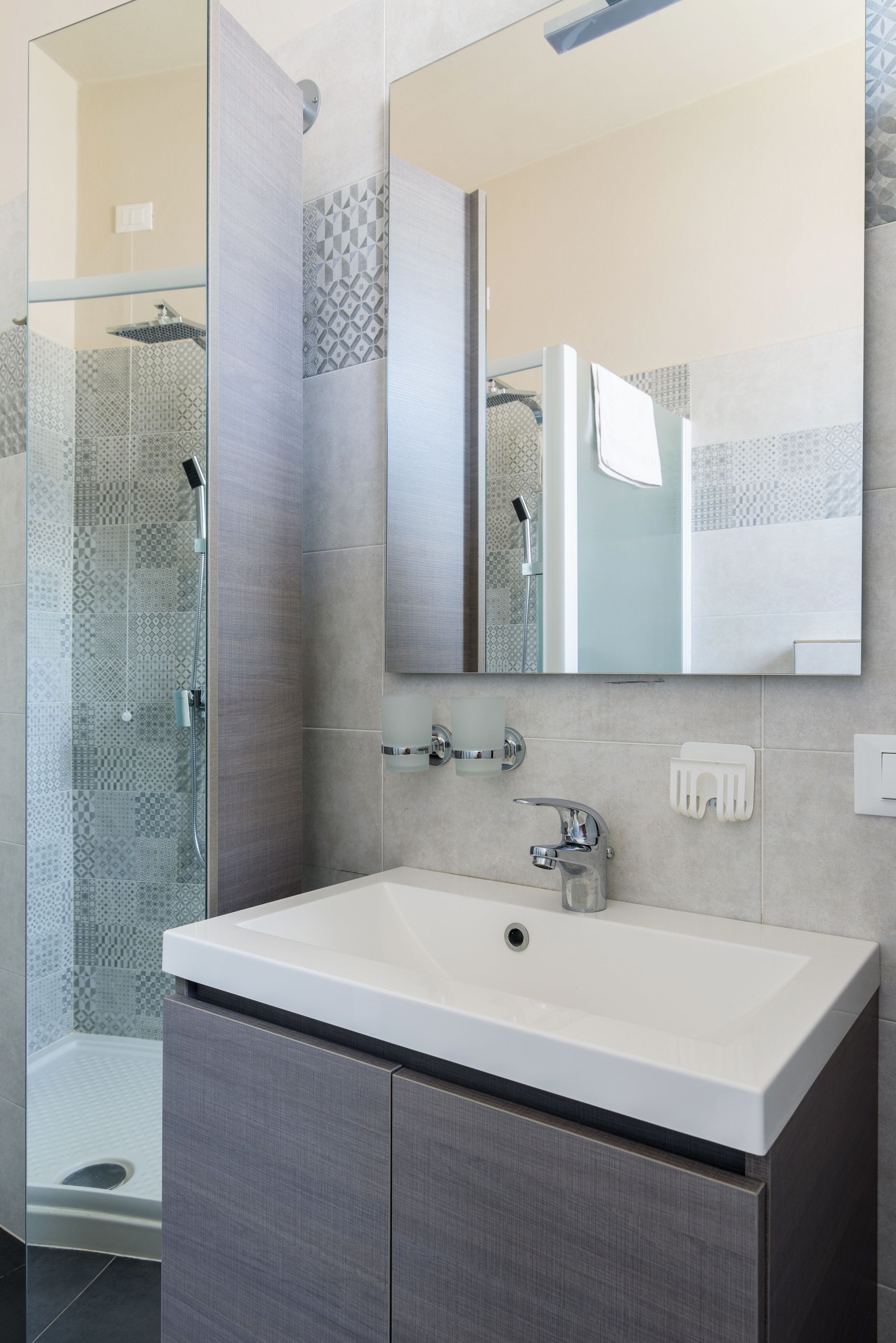 A modern bathroom with a large mirror, a white sink, and a shower area.