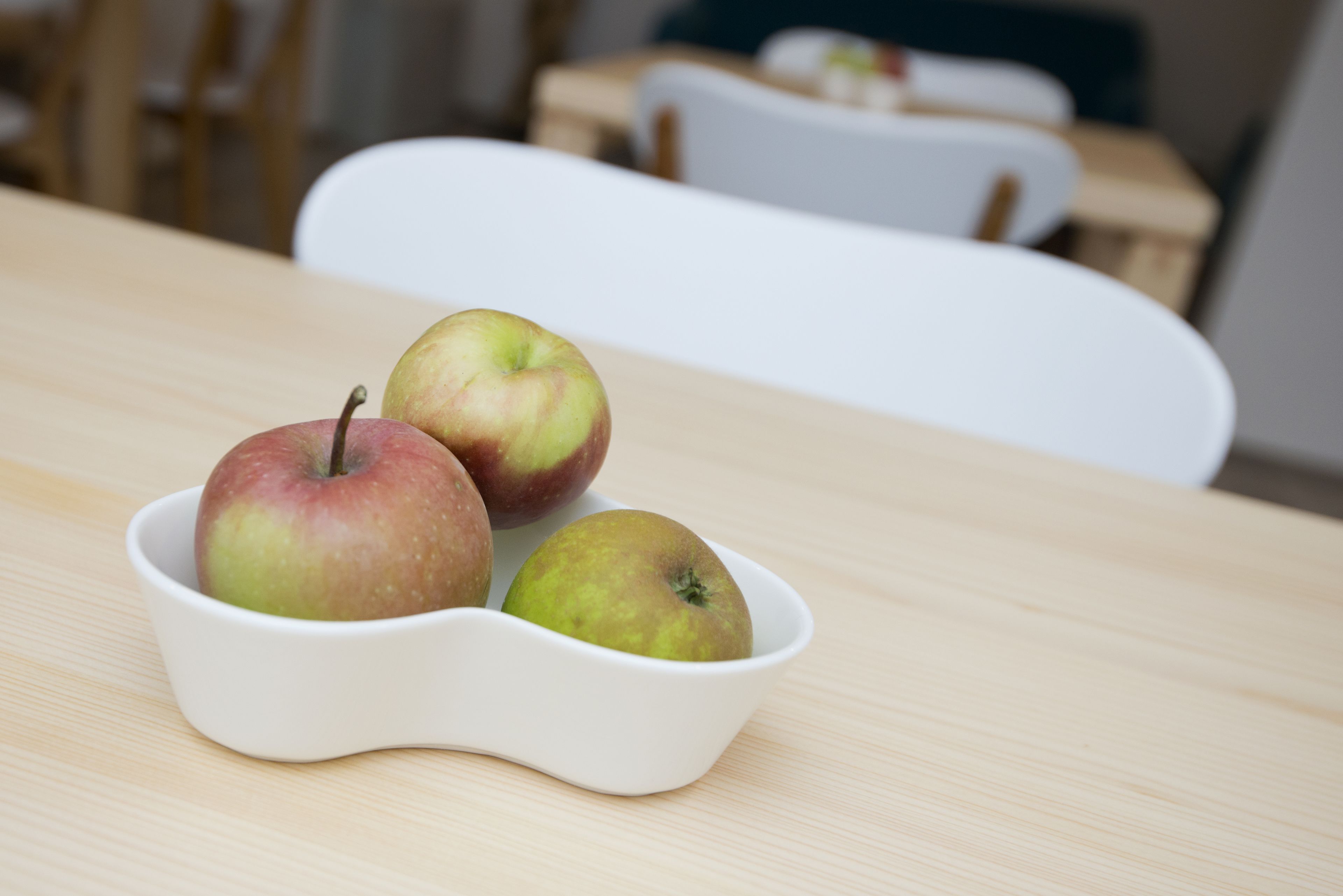 A white bowl with three apples on a wooden table.