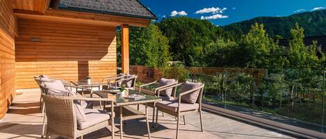 A wooden cabin with a balcony featuring wicker furniture and a glass railing.