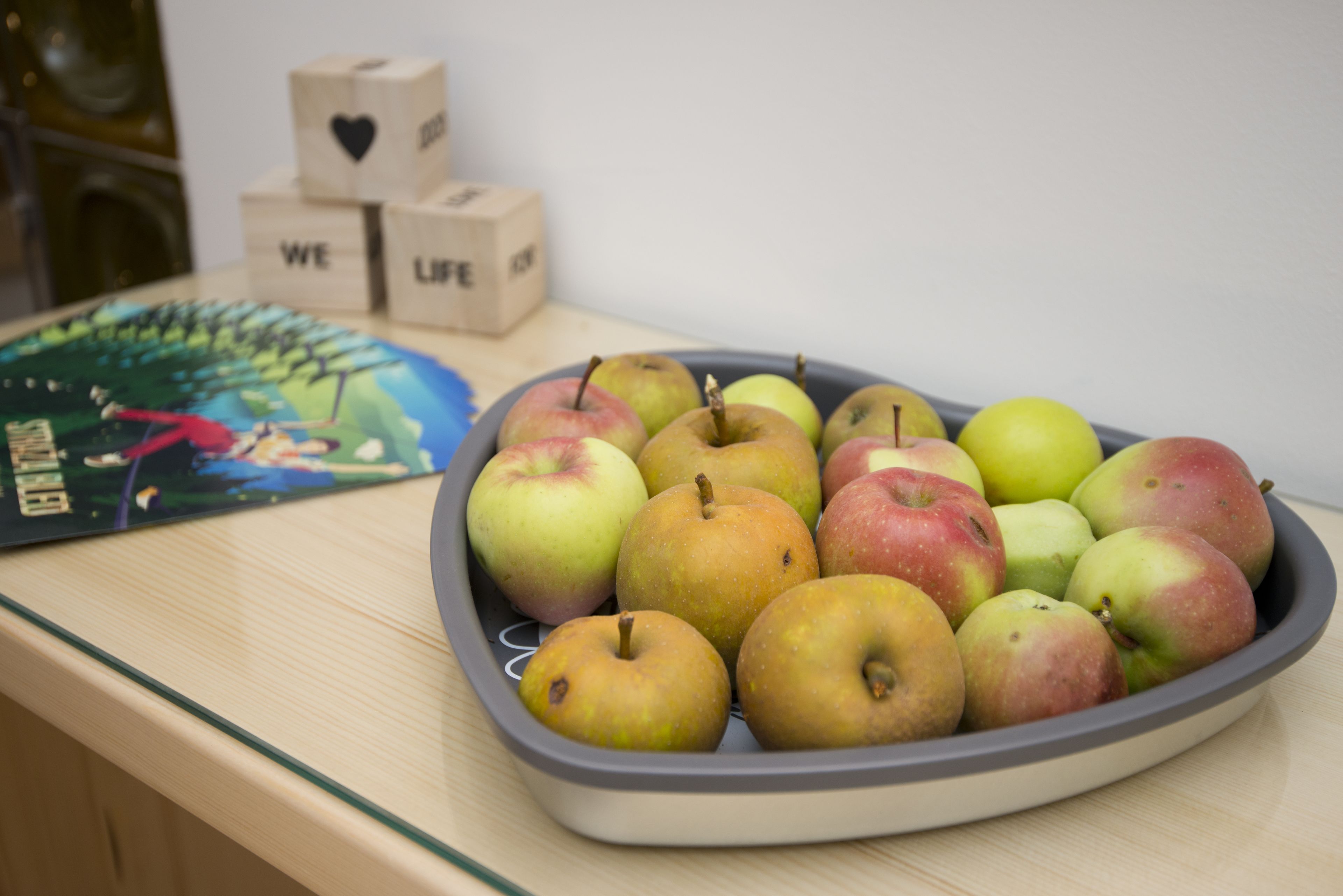 Un plateau de pommes sur une table, avec un jeu de société et des blocs de bois portant des mots.