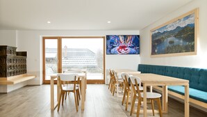A modern dining area with a wooden table and chairs, a blue sofa, and a large window with a view of a building. - Vila Alpina (Bled)